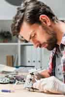 Free photo side view of young male technician repairing helicopter toy on wooden desk