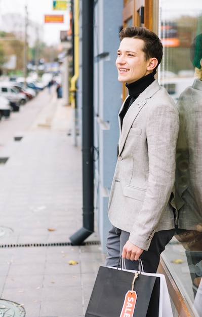 Free photo side view of a young man in fashionable suit holding shopping bags standing on street