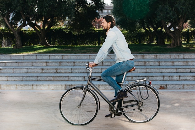 Free photo side view of a young man riding bicycle in the park