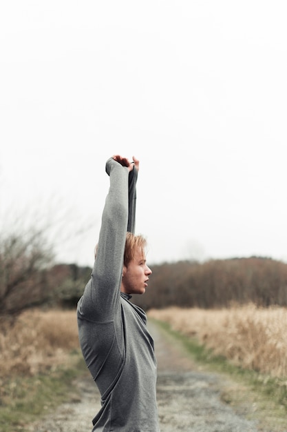 Side view of young man standing in field stretching his hand