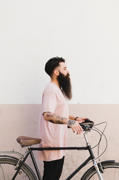 Side view of a young man standing with his bicycle against wall