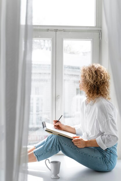 Side view of a young woman drawing at home near the window