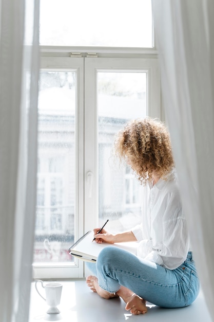 Free Photo side view of a young woman drawing at home near the window