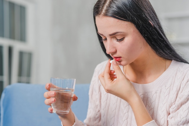 Side view of a young woman holding glass of water taking medicine