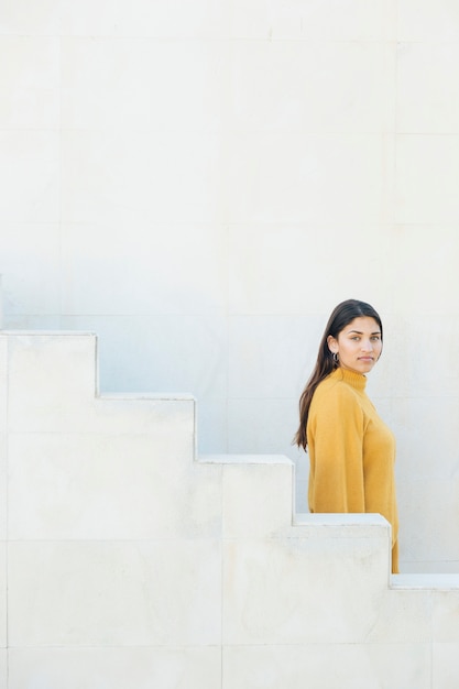 Free Photo side view of a young woman looking at camera standing near staircase