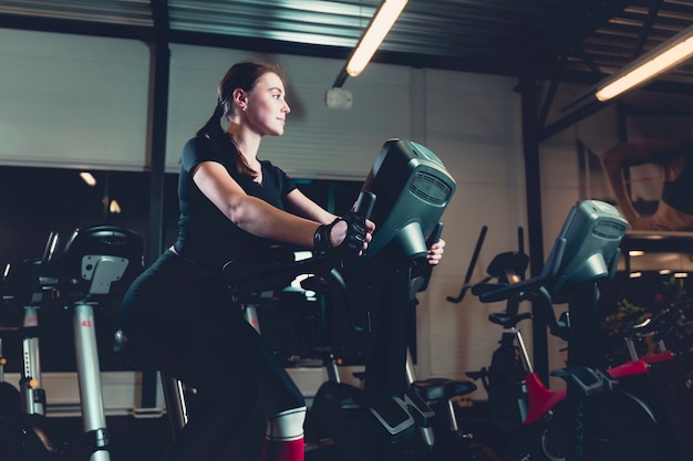 Side view of a young woman riding on exercise bike in gym