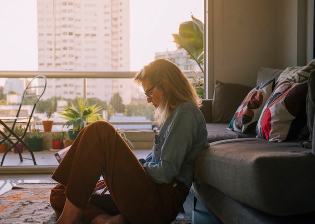 Free photo side view of a young woman sitting on carpet using laptop at home