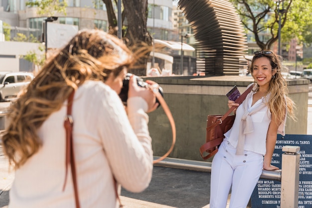 Free photo side view of a young woman taking photo of her friend leaning on railing