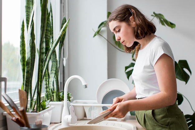 Free photo side view young woman washing dishes