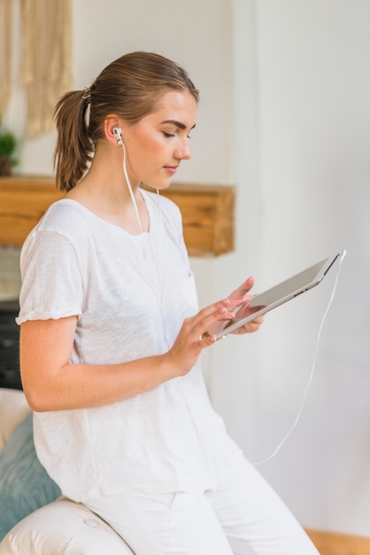 Side view of young woman with earphone browsing digital tablet