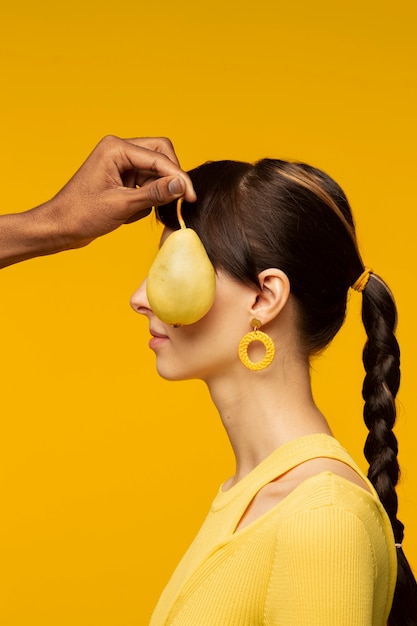 Free photo side view of young woman with pear covering her face