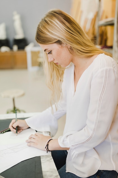 Side young woman sketching on paper with pencil on the workbench