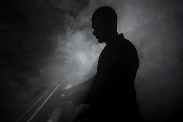 Free photo sideways artist playing piano smoke and shadows effects