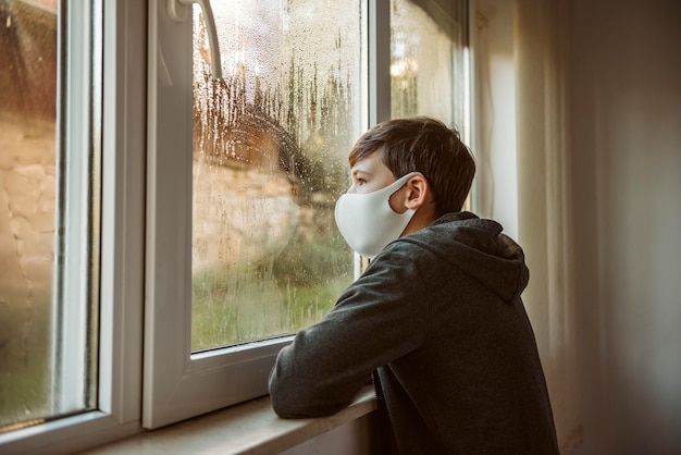 Free photo sideways boy with face mask looking through the window