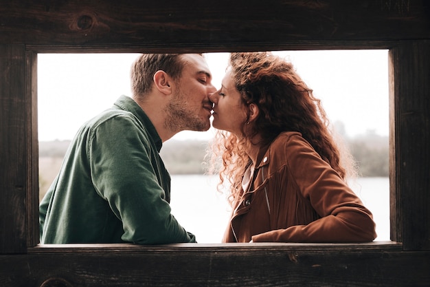 Free photo sideways couple kissing next to a wooden window