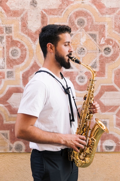 Free photo sideways man medium shot playing the saxophone with geometric background