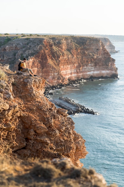 Free Photo sideways man sitting on a coast and enjoying the view