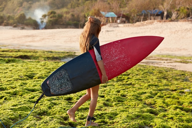 Sideways shot of professional goofy carries surfboard with leash