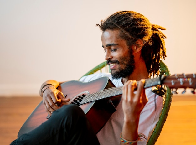 Free Photo sideways smiley man with dreads playing the guitar