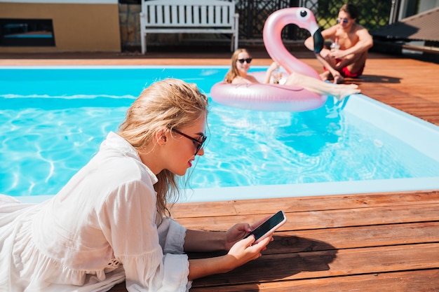 Free photo sideways woman checking her phone at the pool