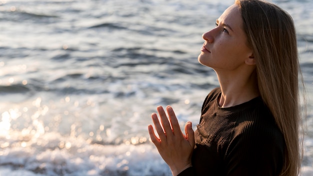 Free photo sideways woman meditating on the beach