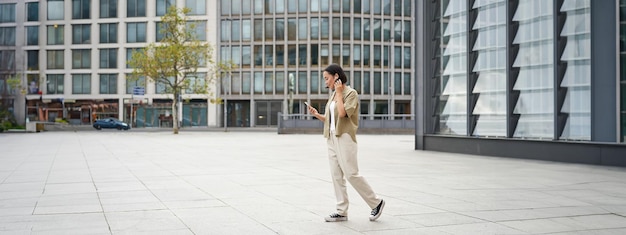 Free Photo silhouette of asian woman walking on street in wireless headphones holding smartphone