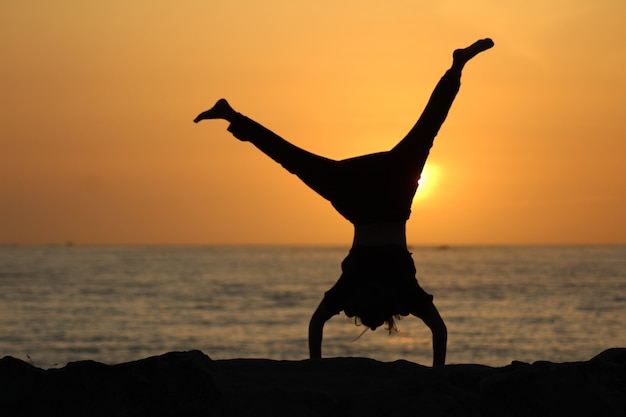 Free Photo silhouette of a female doing a cartwheel with a blurred sea and a clear sky