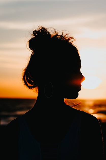 Free photo silhouette of a female standing on the coast of the sea with a beautiful sunset