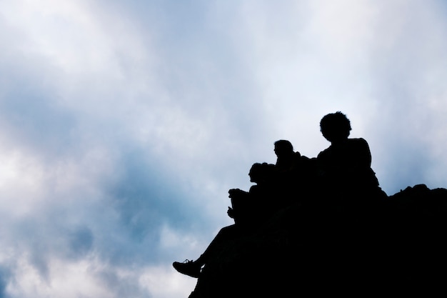 Free Photo silhouette of friends sitting on rock against blue sky