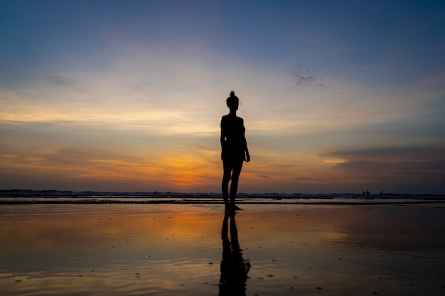 Free photo silhouette of a girl standing in the water on a beach as the sun goes down