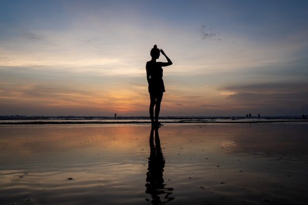 Free photo silhouette of a girl standing in the water touching her hair on a beach