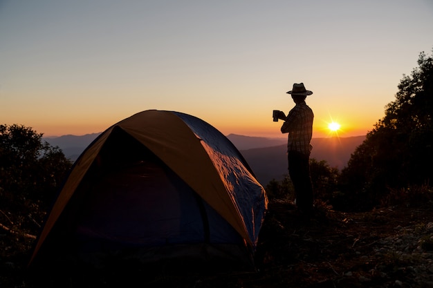 Silhouette of Happy man with holding coffee cup stay near tent around mountains 