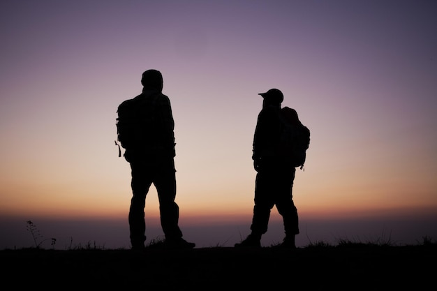 Free photo silhouette of hiker men with backpack stay on cliff and think on the top mountain at sunset travel lifestyle wanderlust adventure concept summer vacations outdoor