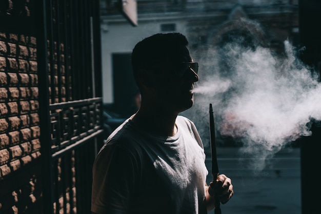 Silhouette of hookah maker blowing smoke in the dark.