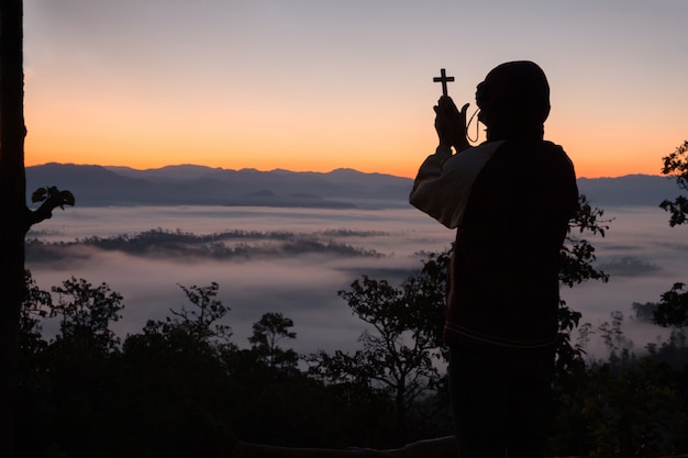 Free photo silhouette of human hand holding the cross, the background is the sunrise