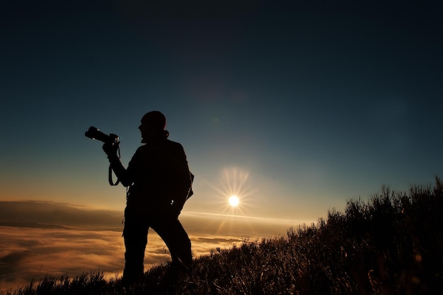 Free photo silhouette of man photographer with camera on hand background mountains on sunset with fog amazing shot of beauty world and human