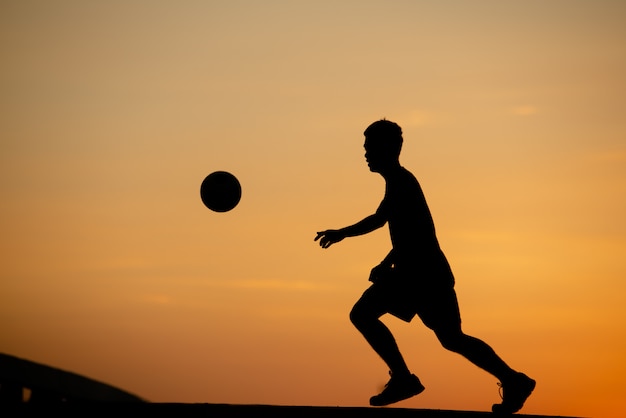 Free photo silhouette of a man playing soccer in golden hour, sunset.