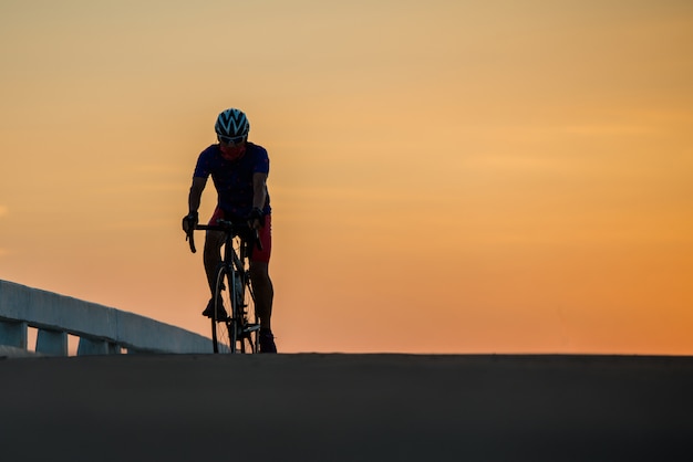 Free photo silhouette of a man rides a bike at sunset.orange-blue sky background.