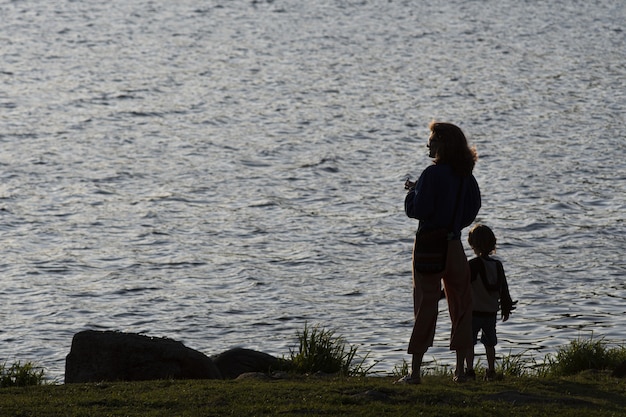 Free photo silhouette of a mother and her son against a lagoon at sunset