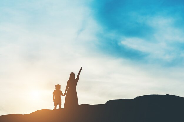 Silhouette of mother with her daughter standing and sunset