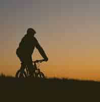 Free photo silhouette of a person riding a bicycle on a field during a sunset