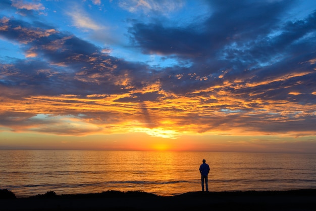 Silhouette of a person standing on a beach under a cloudy sky during a breathtaking sunset