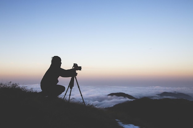 A silhouette of a photographer setting up the camera to shoot the sea of clouds during sunset