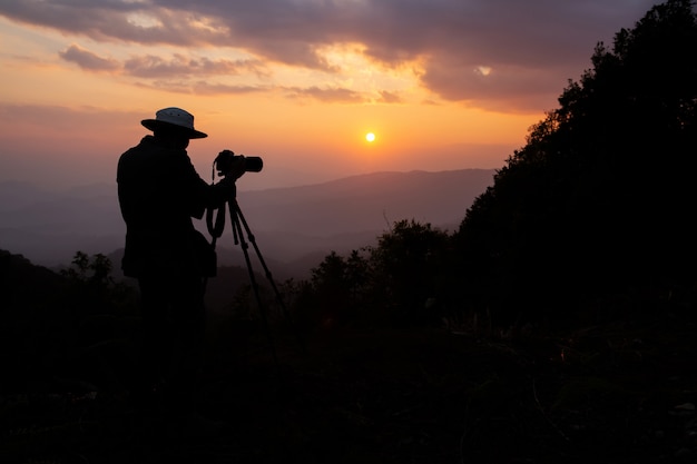 silhouette of a photographer who shoots a sunset in the mountains