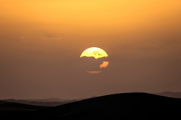 Silhouette of sand dunes with the sun behind a cloud