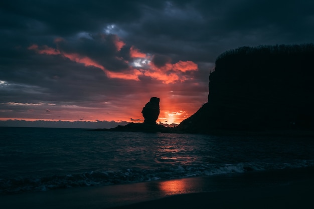 Silhouette of a sea stack against a colorful setting sun at New Caledonia