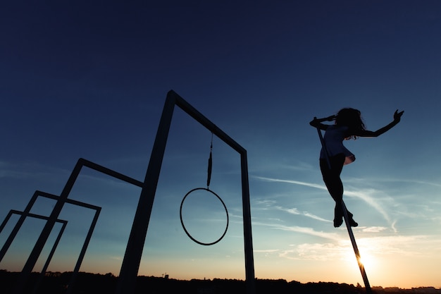 Silhouette of sexy pole dancer performing on roof at sunset