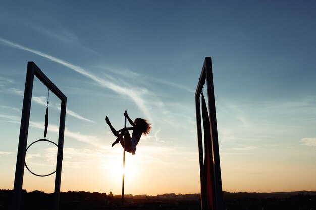 Silhouette of sexy pole dancer performing on roof at sunset