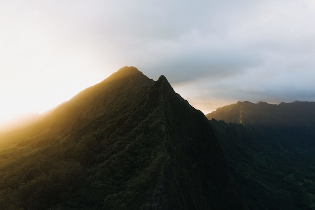 Free photo silhouette shot of a steep mountain with a sunset in a cloudy blue sky