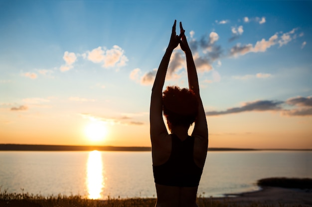 Free Photo silhouette of sportive girl practicing yoga in field at sunrise.